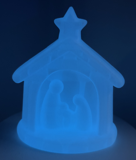 Das Bild zeigt eine kleine, halbtransparente Weihnachtskrippe, die in einem sanften Blau leuchtet.
