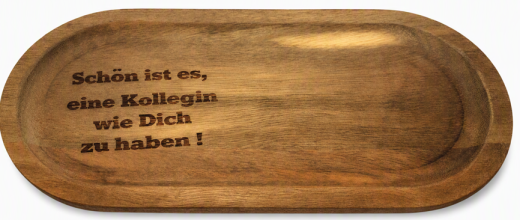 Das Bild zeigt einen elegant gravierten Holz‑Tassenuntersetzer auf einem Holztablett. Die Gravur „Schön ist es, eine Kollegin wie Dich zu haben!“ ist klar und sauber ausgearbeitet. Daneben steht eine weiße Keramiktasse – dekorativ platziert, jedoch nicht